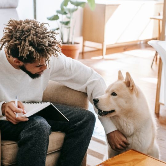 Un homme qui prend des notes sur un carnet en regardant son chien